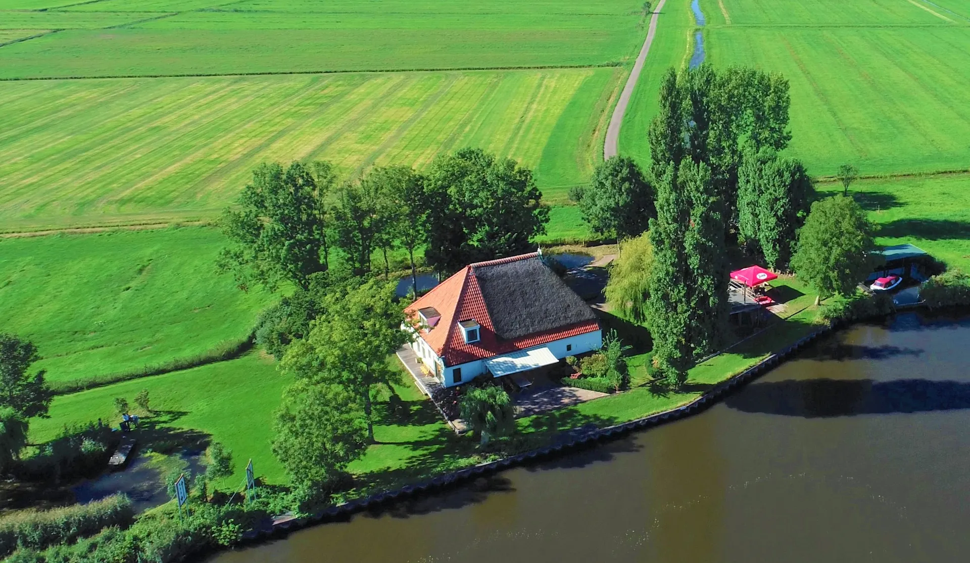 Vrijzicht vanuit de lucht: de rietgedekte woonboerderij aan het Prinses Margrietkanaal, met de eigen haven en het omliggende weiland